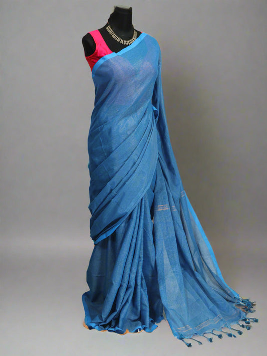 A blue and golden khadi cotton saree with golden stripe patterns and tassels displayed on a mannequin with a red blouse piece. A plant is visible in the background.