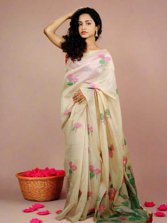 A woman showcasing a beige and pink Muga cotton silk saree with a floral design, paired with a matching pink blouse piece.